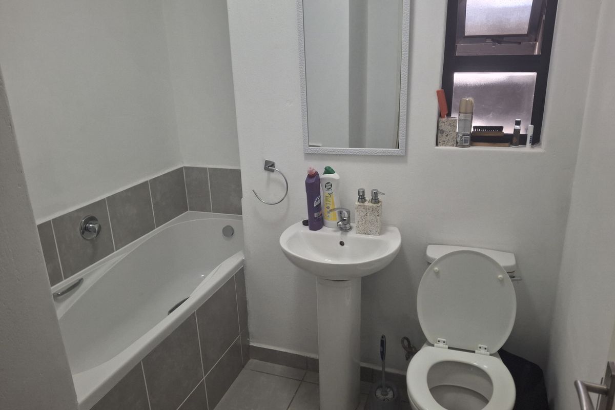 A functional bathroom featuring a pedestal basin, a bathtub with tiled surround, and a standard toilet, finished with neutral floor and wall tiles.