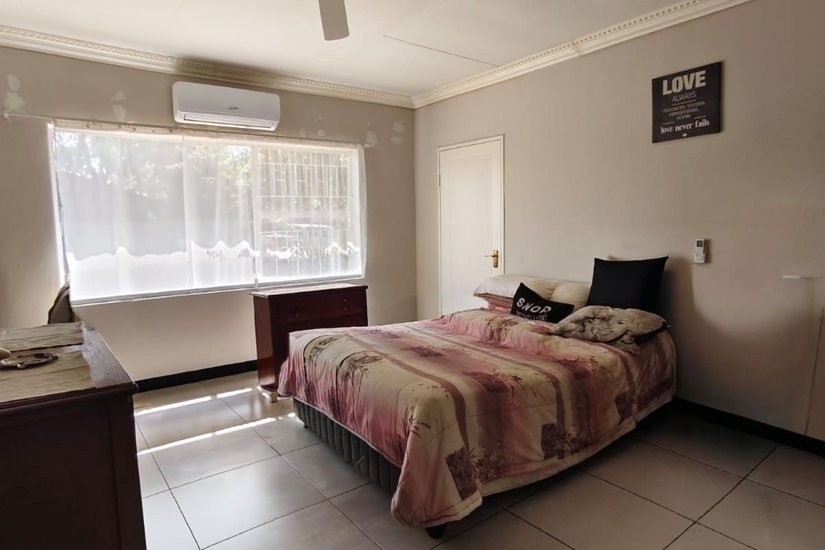 Spacious bedroom featuring tiled flooring, a ceiling fan, and a wall-mounted air conditioning unit.