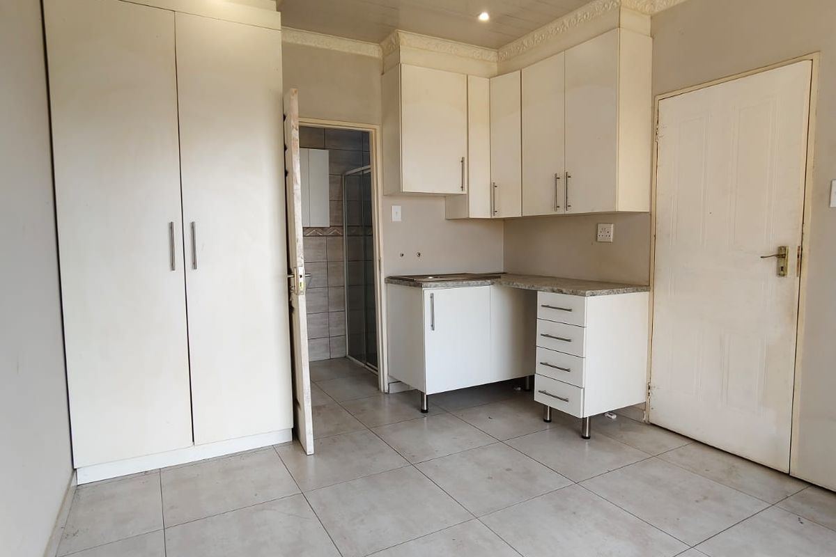 A compact kitchen area featuring white cabinetry, tiled flooring, and a panelled ceiling, with an adjacent doorway leading to a bathroom.