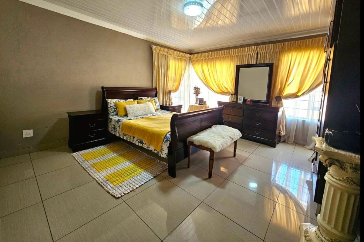 Spacious bedroom featuring large format floor tiles, a glossy panelled ceiling, and expansive windows with integrated curtain tracks.