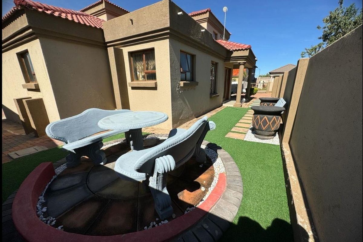 A well-maintained rear garden area featuring a paved circular seating space, artificial lawn, and perimeter boundary wall.