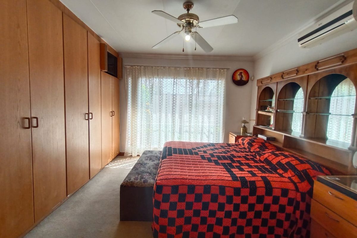 A spacious bedroom featuring extensive built-in wooden cabinetry, a ceiling fan, and a wall-mounted air conditioning unit.