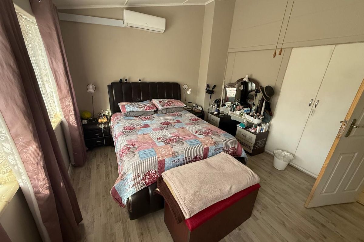 A functional bedroom featuring built-in cupboards, wood-look laminate flooring, and a wall-mounted air conditioning unit.