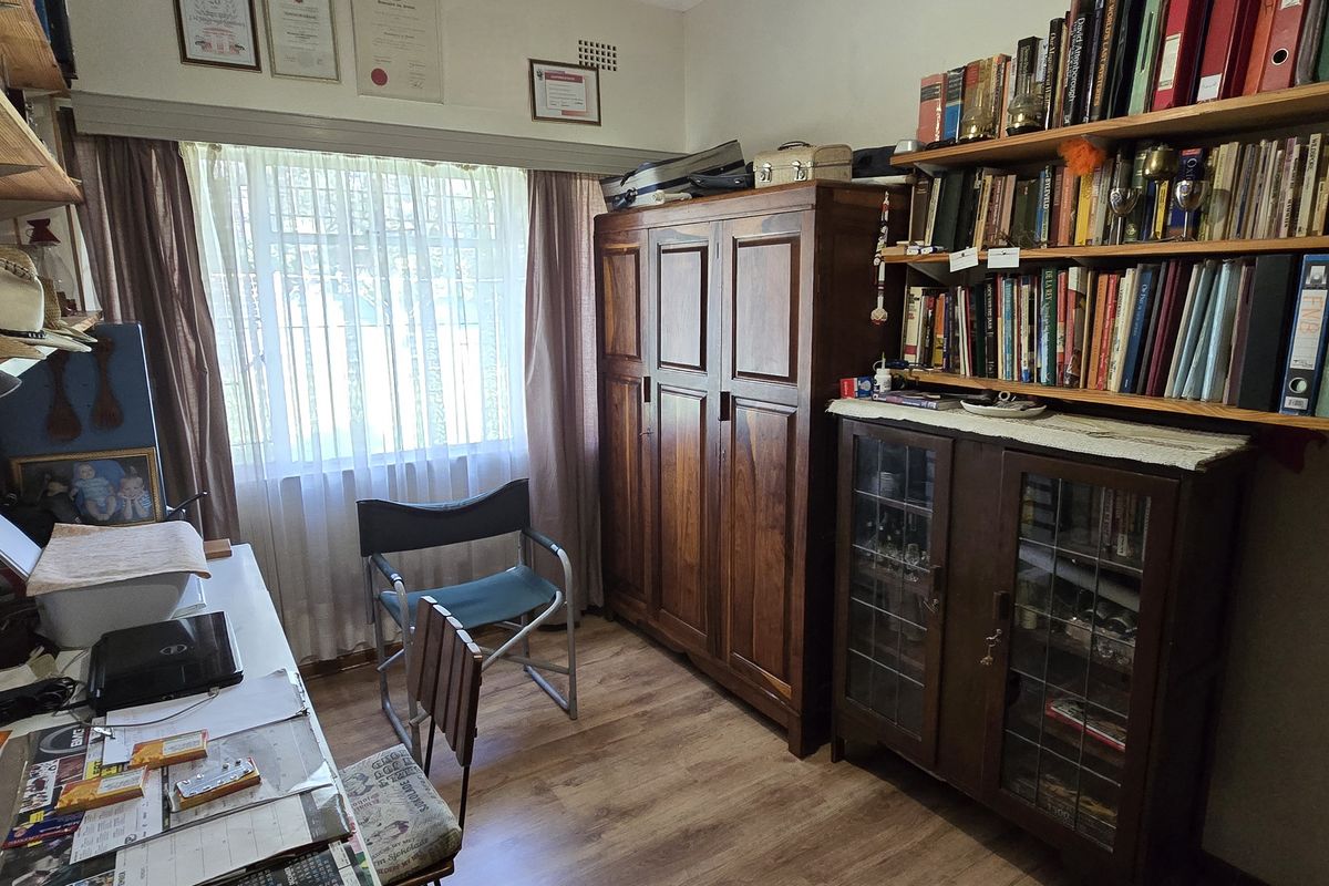 A functional bedroom or home office space featuring wood-look flooring, a large window with curtains, and built-in shelving units.