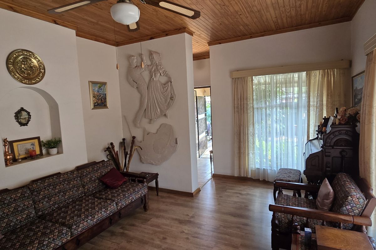 A living room featuring a wood-paneled ceiling, ceiling fan, and a built-in arched wall niche, with large windows providing natural light.