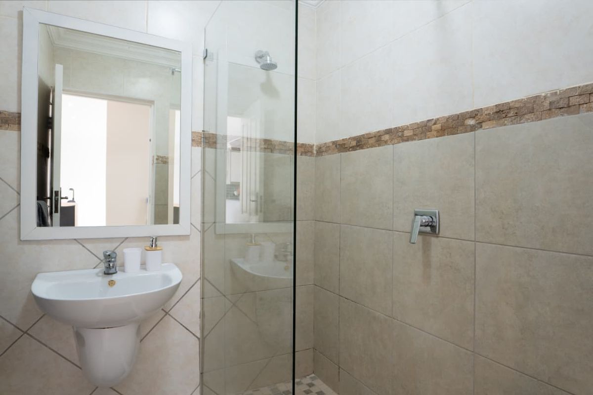 A modern bathroom featuring a wall-mounted basin, a glass-enclosed shower with tiled walls, and a decorative mosaic tile border.