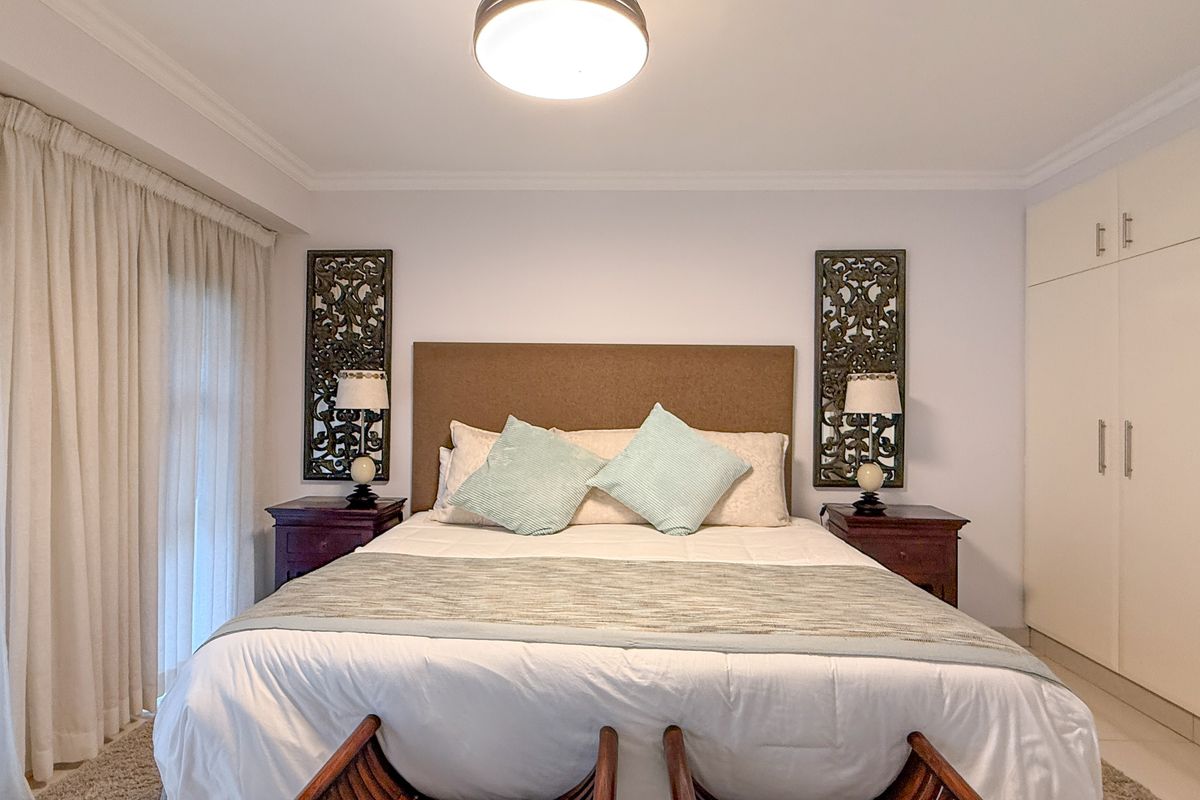 A well-maintained bedroom featuring built-in cupboards, neutral finishes, and direct access to a balcony through floor-to-ceiling curtains.