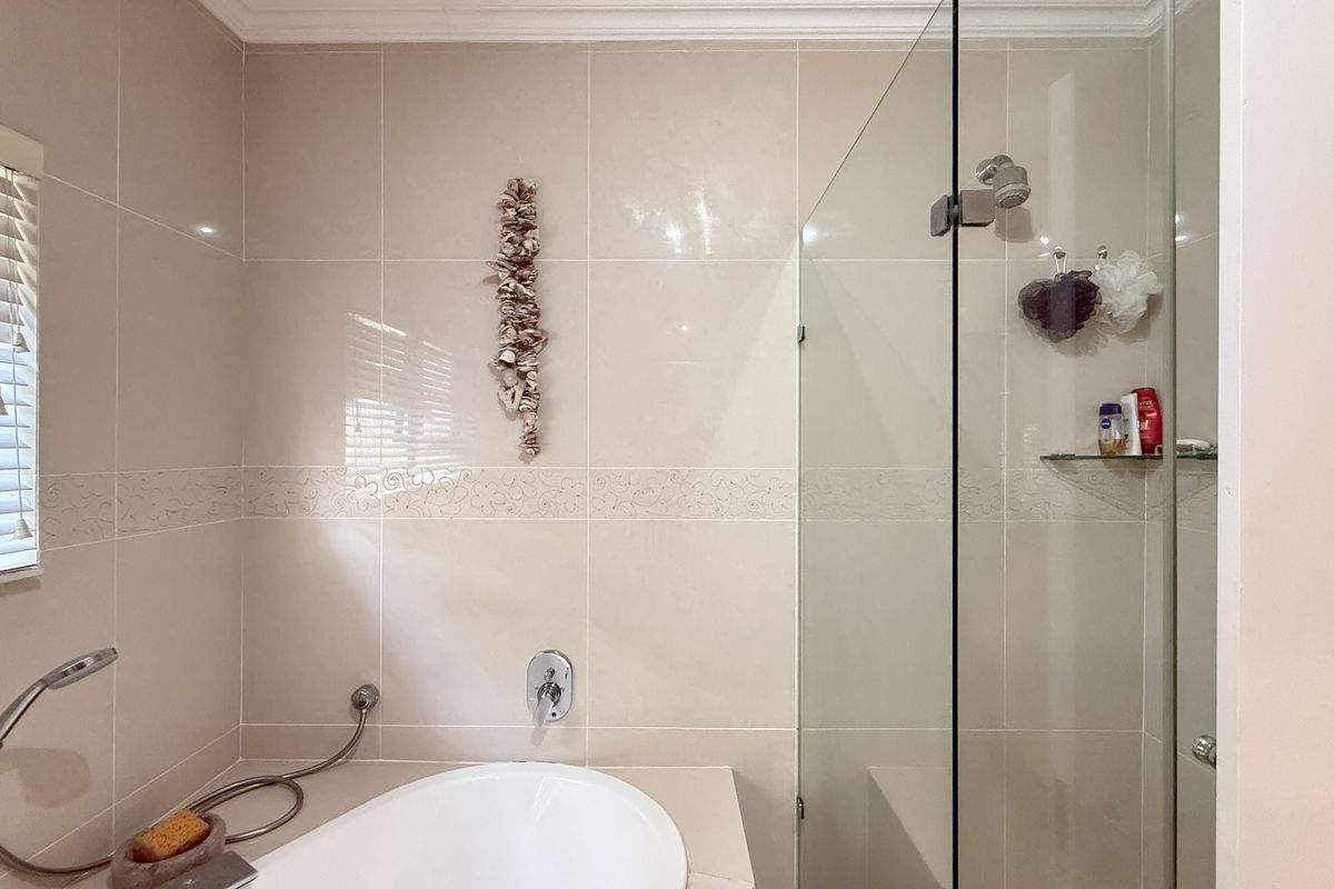 A well-maintained bathroom featuring a built-in bathtub, a separate glass-enclosed shower, and neutral wall tiling with decorative accents.