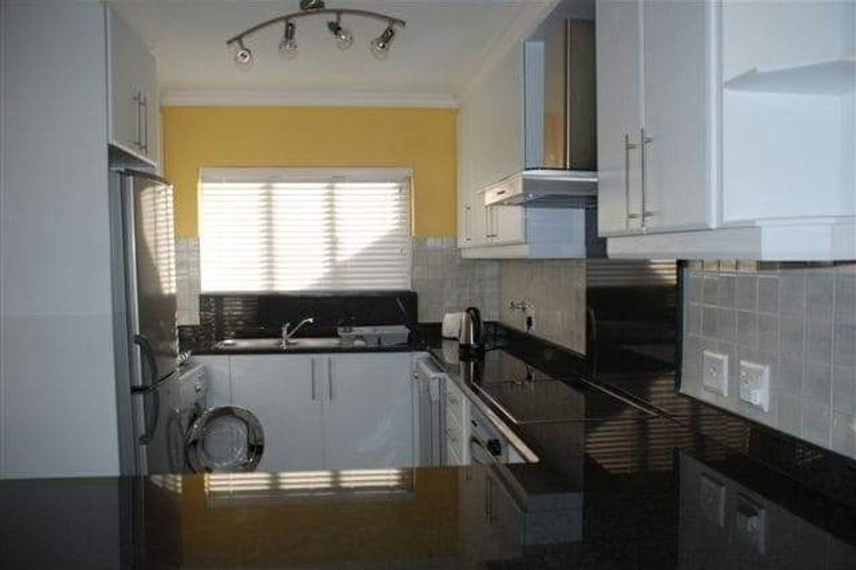 Compact kitchen featuring white cabinetry, dark granite countertops, tiled backsplash, stainless steel extractor fan, and integrated laundry plumbing.