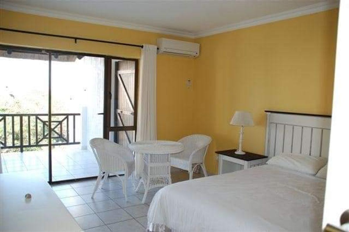 A bedroom featuring tiled flooring, a wall-mounted air conditioning unit, and sliding glass doors providing direct access to an outdoor balcony area.