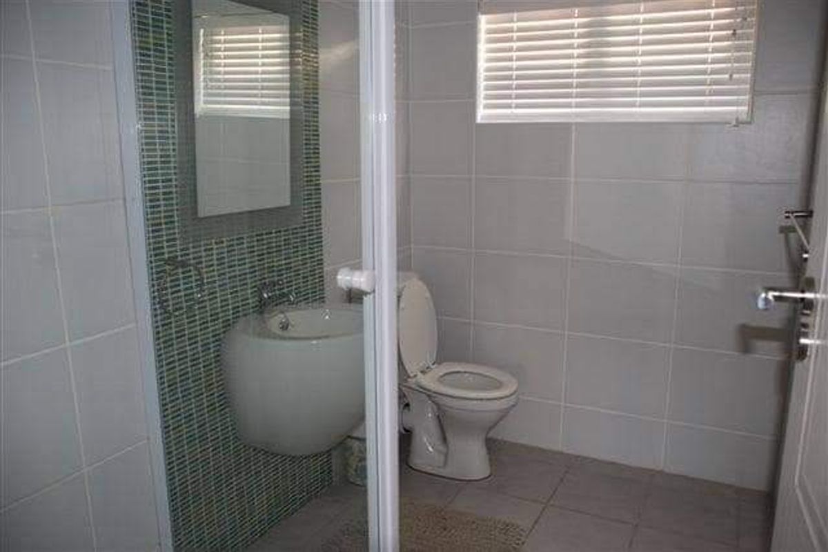 A compact bathroom featuring a wall-mounted basin with mosaic tile backsplash, a standard toilet, and tiled flooring.