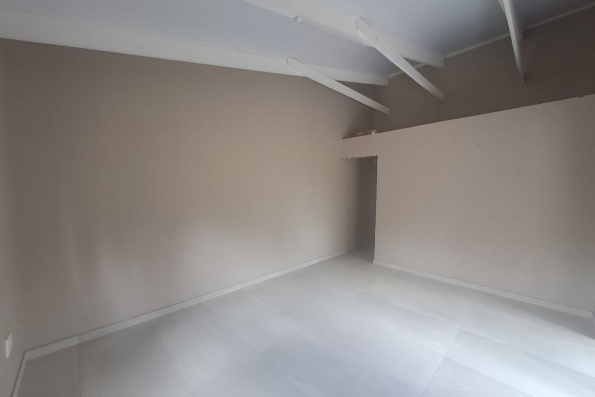 An empty, neutral-toned room featuring high vaulted ceilings with exposed white beams and modern light-colored floor tiles.
