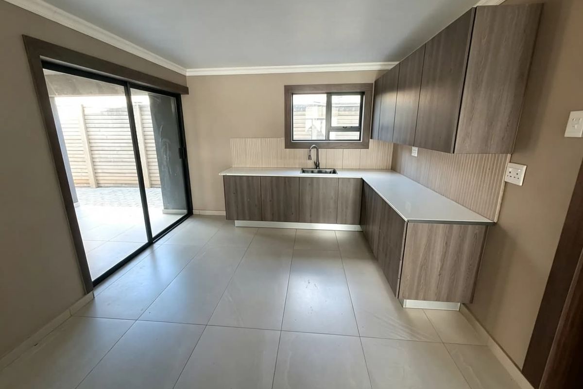 Modern kitchen featuring wood-finish cabinetry, stone countertops, tiled backsplash, and direct access to an outdoor patio area through sliding glass doors.