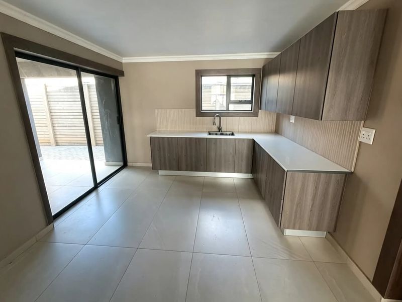 Modern kitchen featuring wood-finish cabinetry, stone countertops, tiled backsplash, and direct access to an outdoor patio area through sliding glass doors.