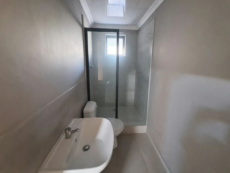 A modern, minimalist bathroom featuring a walk-in shower with a glass screen, pedestal basin, and toilet, finished with neutral wall tones.
