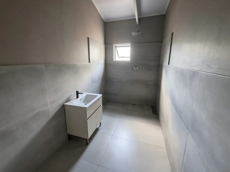 Modern bathroom featuring large format grey wall and floor tiles, a contemporary vanity unit, and a walk-in shower area.