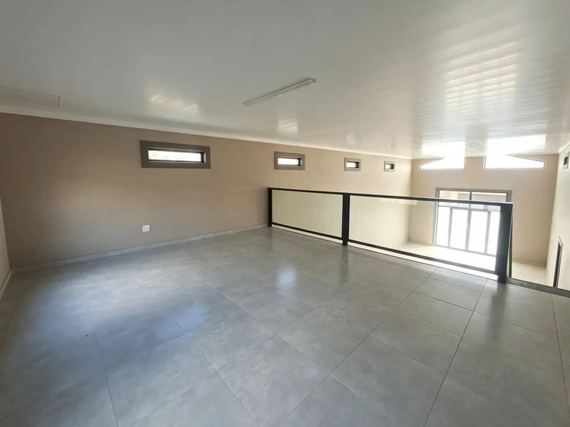 A spacious, empty mezzanine living area featuring modern grey floor tiles, a sleek glass balustrade, and multiple clerestory windows providing natural light.
