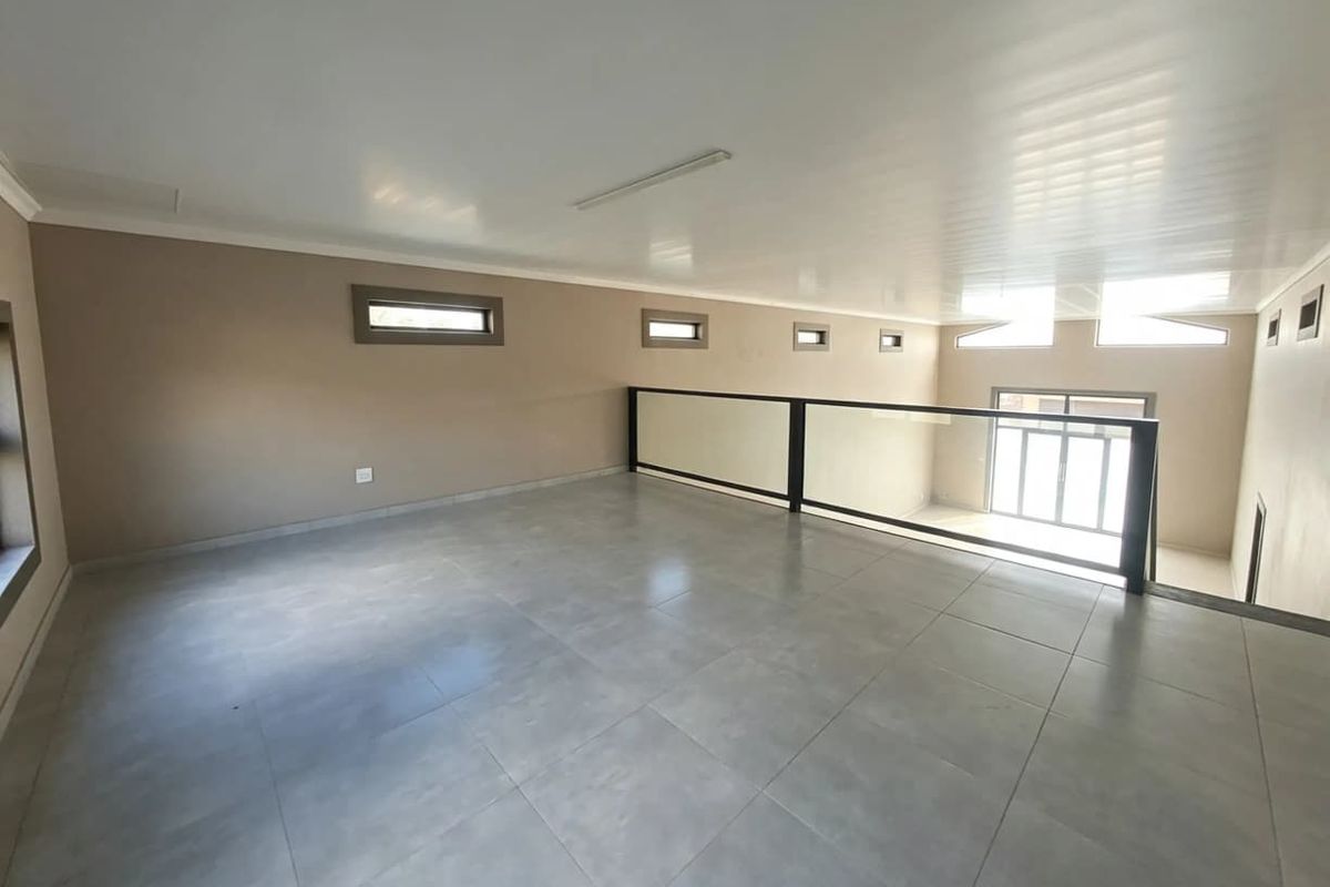 A spacious, empty mezzanine living area featuring modern grey floor tiles, a sleek glass balustrade, and multiple clerestory windows providing natural light.