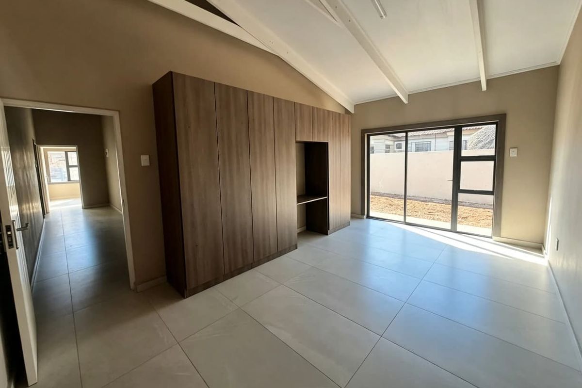 Spacious bedroom featuring modern tiled flooring, built-in cupboards, exposed beam ceiling, and a sliding glass door providing access to the exterior.