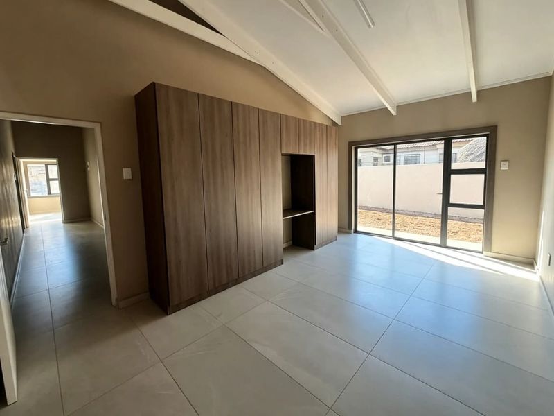 Spacious bedroom featuring modern tiled flooring, built-in cupboards, exposed beam ceiling, and a sliding glass door providing access to the exterior.