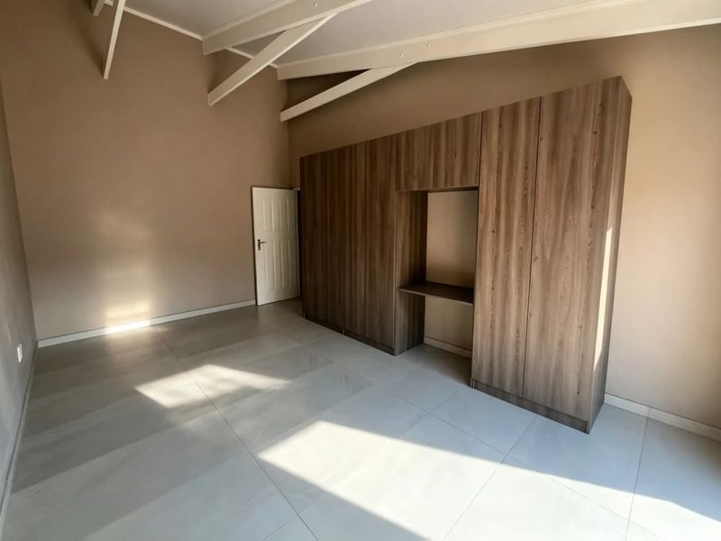 Spacious bedroom featuring neutral tiled flooring, exposed ceiling rafters, and extensive built-in cabinetry with an integrated desk area.