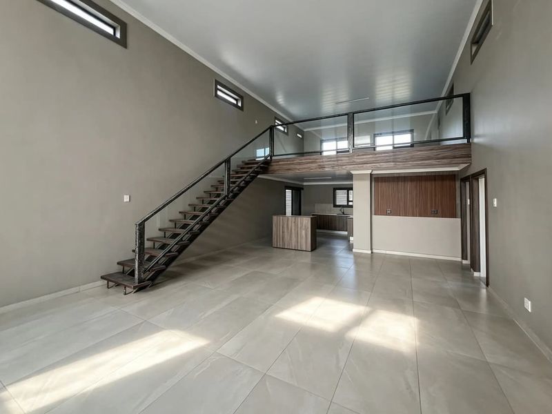 Spacious open-plan living area featuring a modern staircase, mezzanine level with glass balustrade, tiled flooring, and a contemporary kitchen with island.
