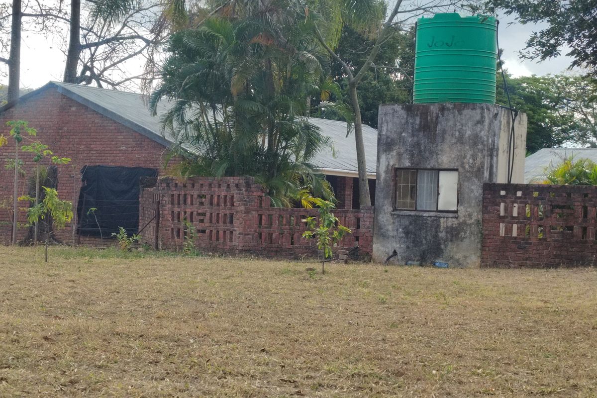 Exterior view of a farm building featuring exposed brickwork, a water tank on a concrete stand, and surrounding garden area.