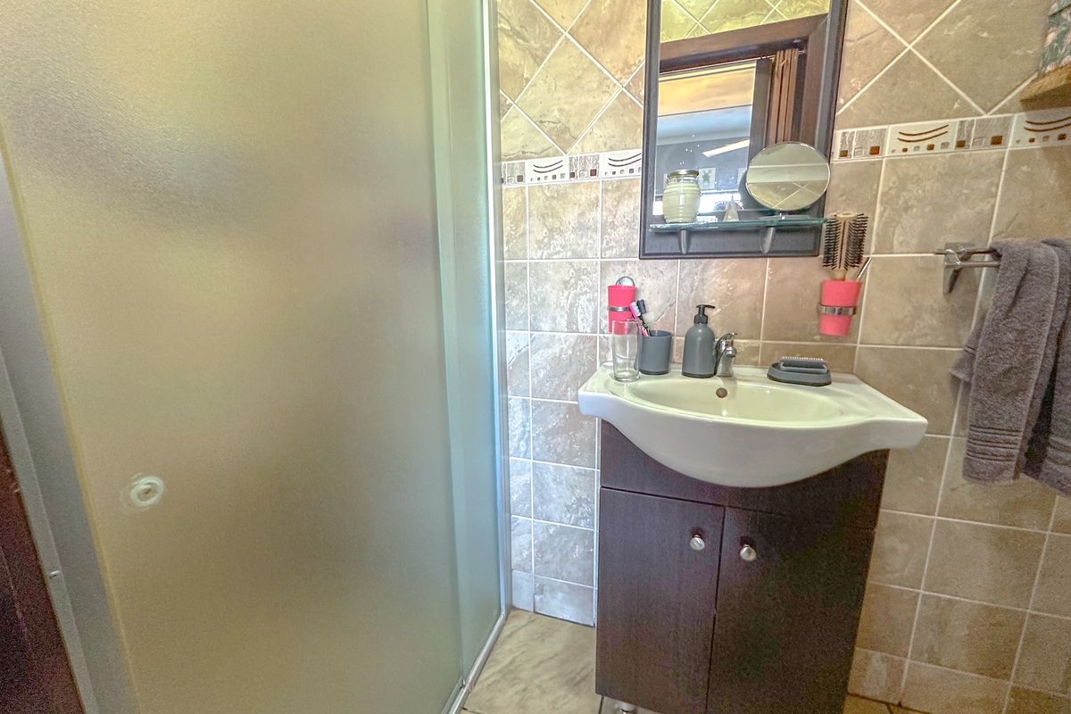 Compact bathroom featuring a corner vanity unit with integrated basin, wall-mounted mirror, and a glass-enclosed shower stall with neutral wall and floor tiling.
