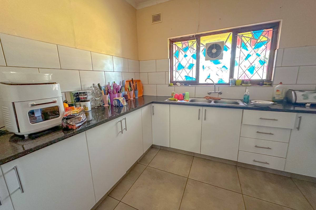 A functional kitchen featuring white cabinetry, dark granite countertops, a double basin sink, and a distinctive stained glass window with an integrated extractor fan.