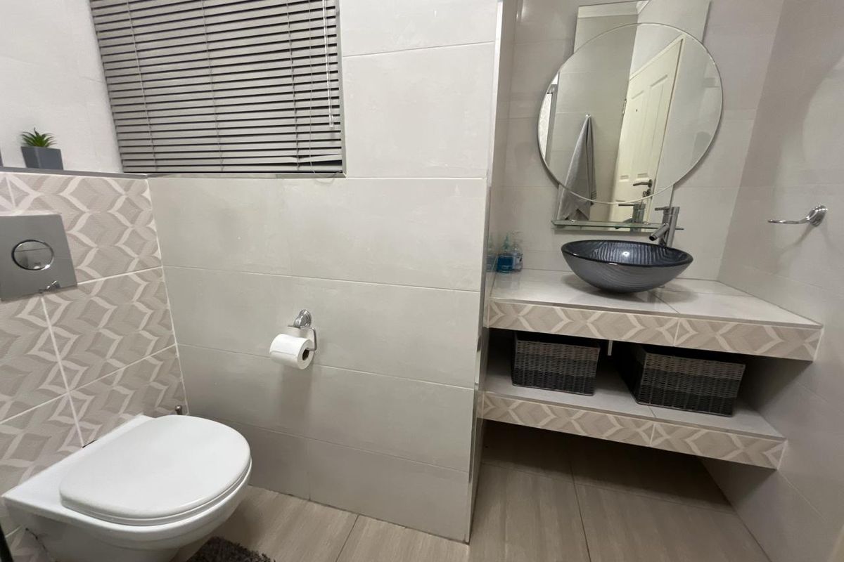 Modern bathroom featuring a wall-mounted toilet, a vessel sink on a tiled vanity, and a circular mirror with neutral wall and floor tiling.