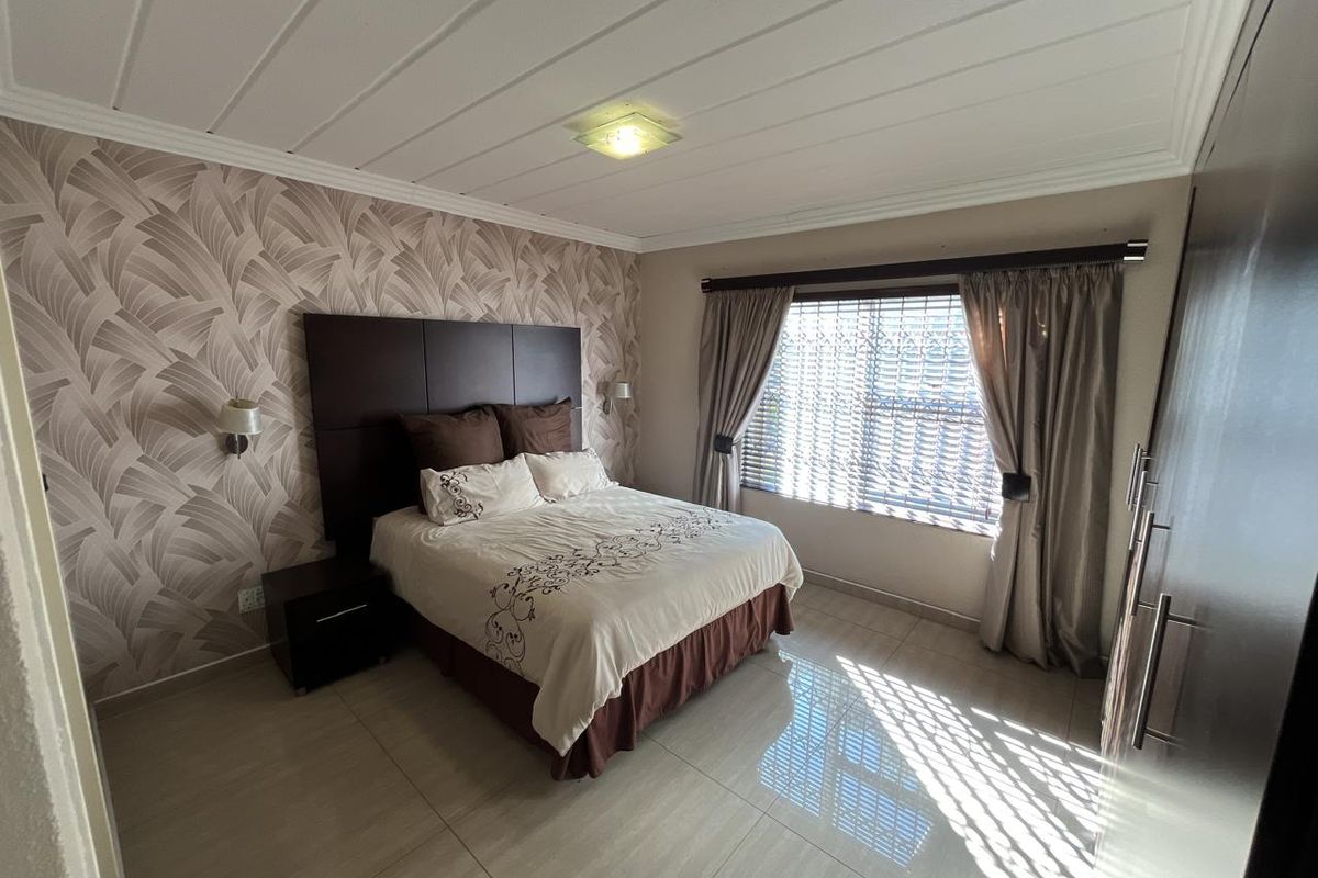 A well-maintained bedroom featuring tiled flooring, a patterned feature wall, and built-in cabinetry, offering a clean and functional living space.