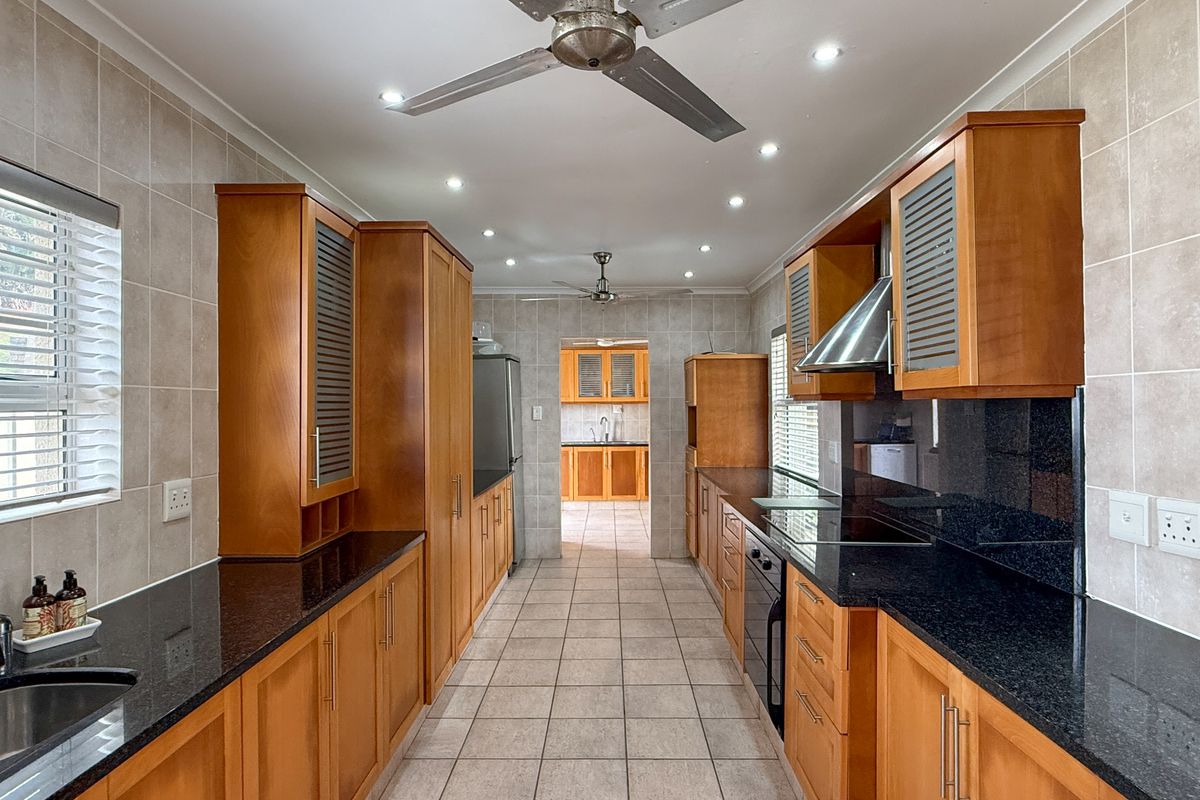 A galley-style kitchen featuring wooden cabinetry, dark granite countertops, tiled flooring, a built-in oven, and a stainless steel extractor fan.
