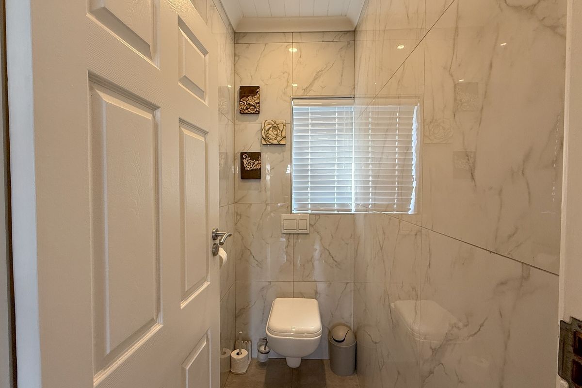 A compact, modern bathroom featuring floor-to-ceiling marble-look wall tiles, a wall-mounted toilet, and a window with fitted blinds.