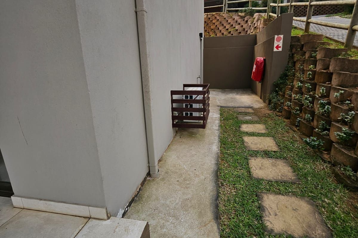 A side pathway featuring a concrete walkway, tiered retaining walls, and a landscaped garden area alongside the townhouse structure.