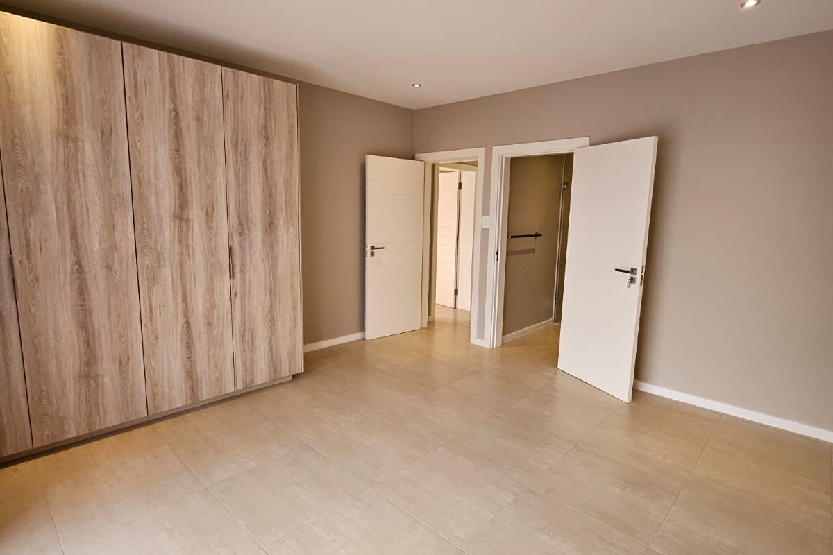 Spacious bedroom featuring neutral tiled flooring, modern recessed downlighting, and extensive built-in wooden cabinetry.