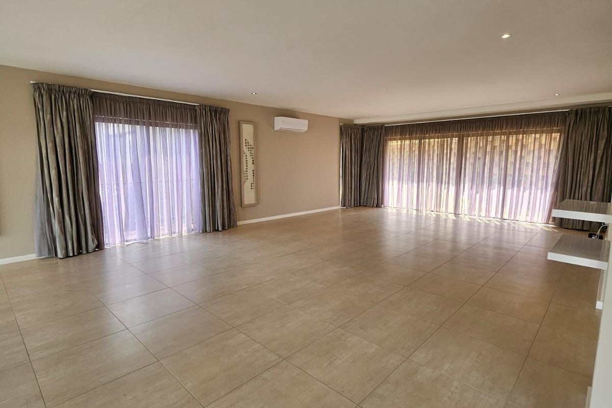 Spacious, open-plan living area featuring large format floor tiles, recessed lighting, split-system air conditioning, and dual sliding glass doors providing ample natural light.
