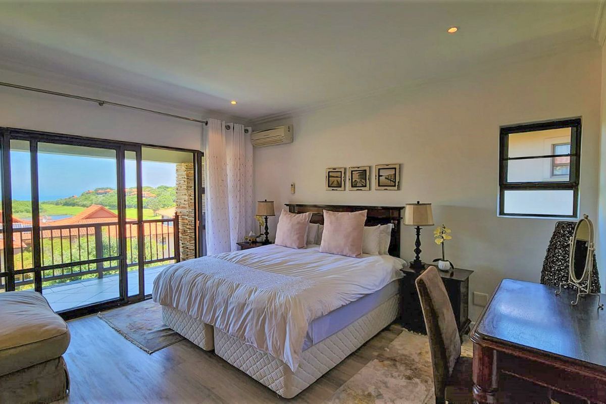 Spacious bedroom featuring wood-look flooring, recessed lighting, a wall-mounted air conditioning unit, and large sliding glass doors opening onto a private balcony with views.