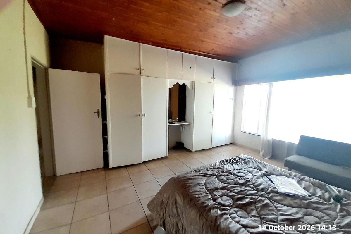 A bedroom featuring tiled flooring, a timber ceiling, and extensive built-in cupboard storage with an integrated vanity area.