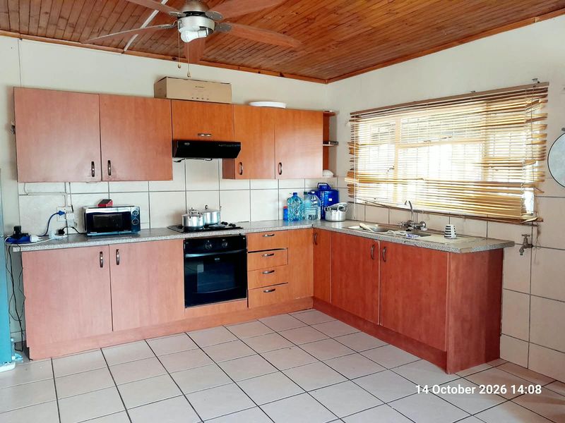 Functional kitchen featuring wooden cabinetry, built-in oven, hob, extractor fan, and tiled flooring with a timber ceiling finish.