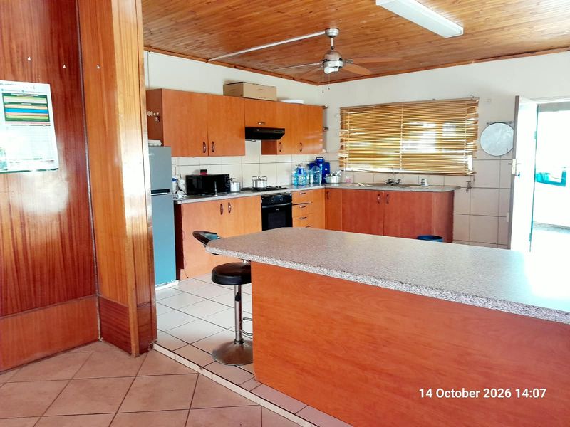 A functional kitchen featuring wooden ceilings, laminate cabinetry, a built-in oven with extractor, and a central breakfast bar with tiled flooring.