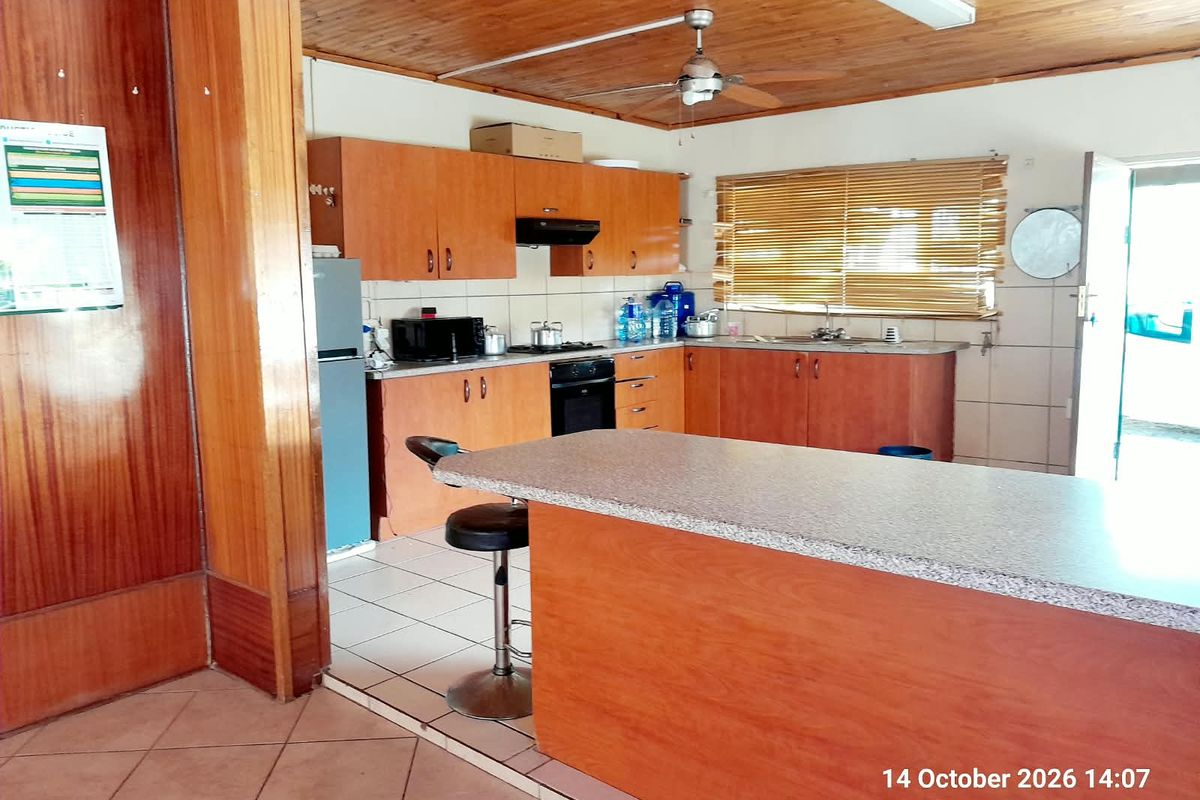 A functional kitchen featuring wooden ceilings, laminate cabinetry, a built-in oven with extractor, and a central breakfast bar with tiled flooring.