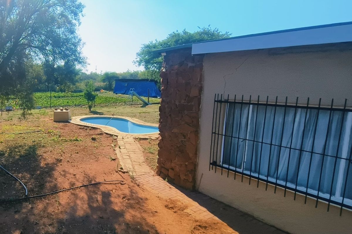 Rear view of the property featuring a swimming pool, stone-clad wall section, and paved pathway leading through the garden area.