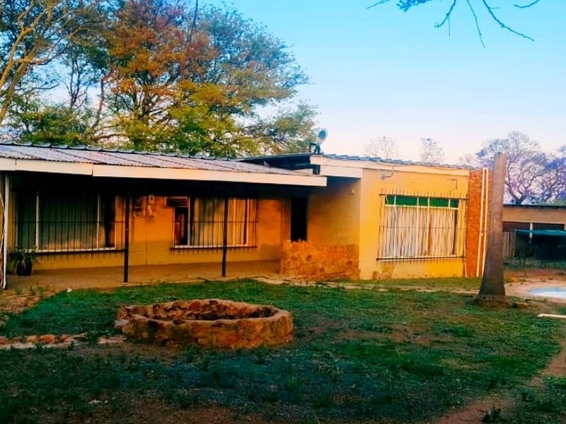 Rear view of the farmhouse featuring a covered patio, swimming pool, and a stone fire pit set within a spacious garden area.