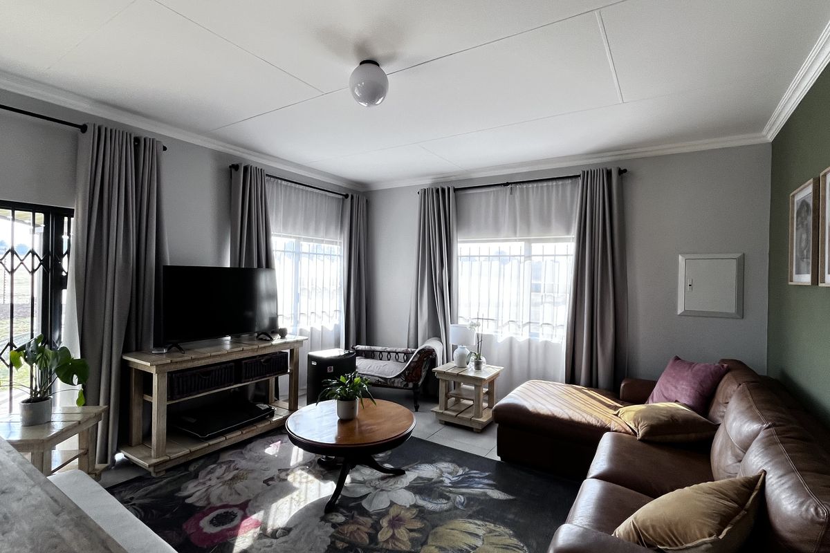 A comfortable living room featuring tiled flooring, large windows with security bars, and neutral wall finishes, providing a bright and inviting space.