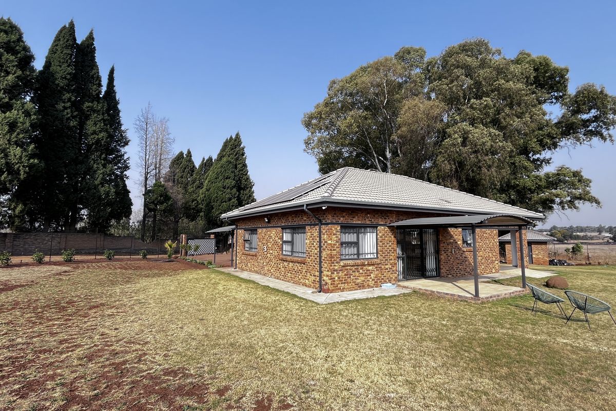 A well-maintained brick farmhouse featuring a tiled roof, solar panels, and a covered patio area set within a spacious, landscaped garden.