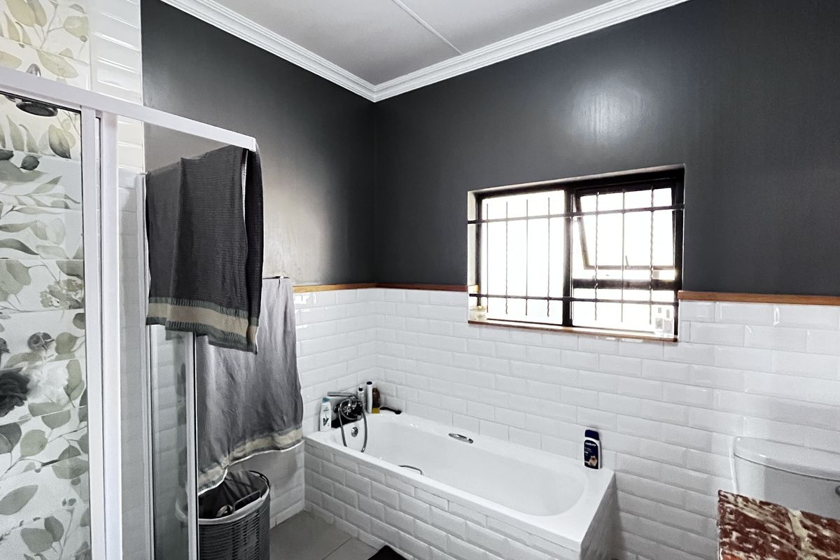 A modern bathroom featuring a white bathtub, a glass-enclosed shower with decorative tiling, and contrasting dark grey walls with white subway tile wainscoting.