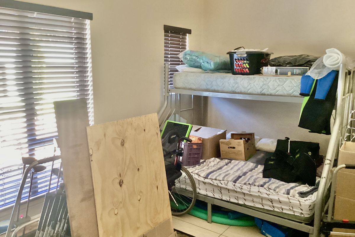 A bedroom featuring tiled flooring and horizontal window blinds, currently utilized for storage.