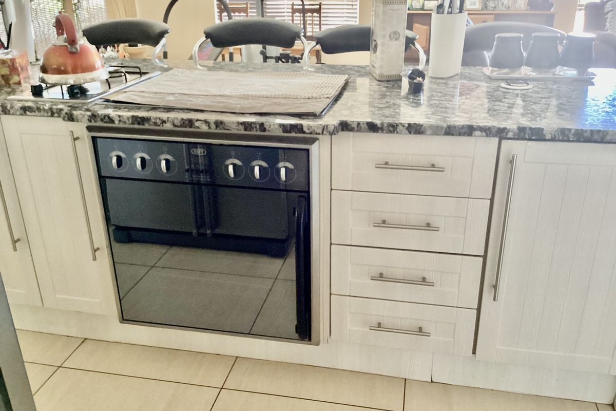 A kitchen island featuring a built-in oven, gas hob, granite countertop, and white cabinetry with modern hardware.