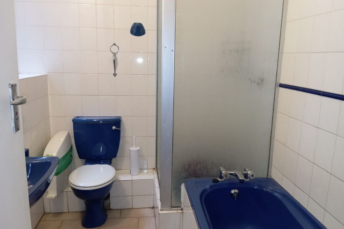 A dated bathroom featuring a blue bathtub, matching blue toilet, and a separate shower enclosure with tiled walls.