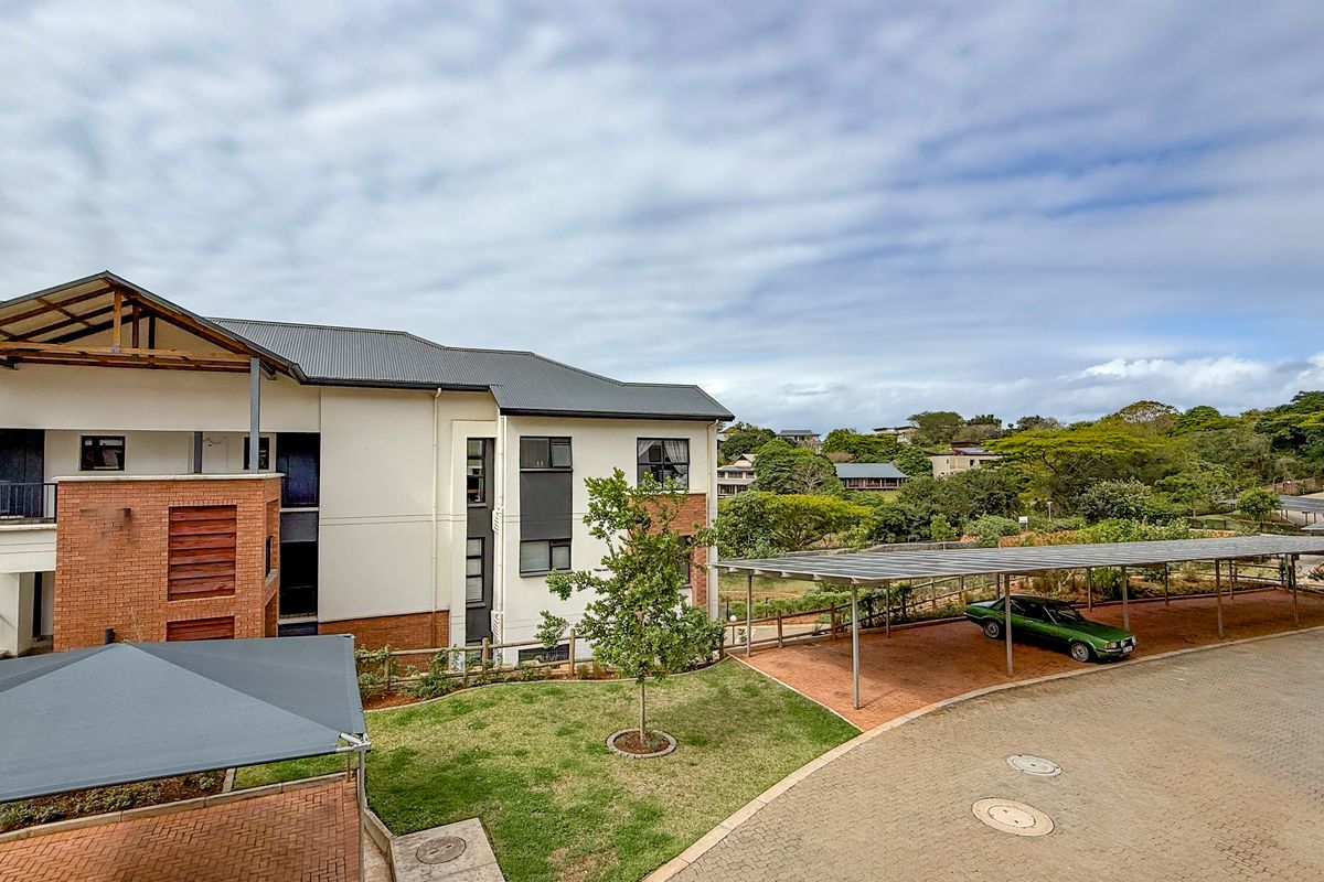Elevated view of the apartment complex grounds, featuring paved parking areas with covered carports, landscaped garden space, and modern building architecture.